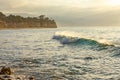 Curling wave forming with transparent green and yellow light moving towards rocks across bay Royalty Free Stock Photo