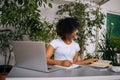 Curly black female student in headphones writing notes, watching webinar, reading paper book studying online using Royalty Free Stock Photo