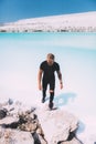 Curly blond man posing at the clear beach. Dressed all black. Awesome background, clear water and sky. Trendy, tropical and