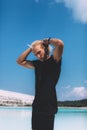 Curly blond man posing at the clear beach. Dressed all black. Awesome background, clear water and sky. Trendy, tropical and