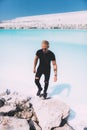 Curly blond man posing at the clear beach. Dressed all black. Awesome background, clear water and sky. Trendy, tropical and
