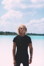 Curly blond man posing at the clear beach. Dressed all black. Awesome background, clear water and sky. Trendy, tropical and