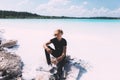 Curly blond man posing at the clear beach. Dressed all black. Awesome background, clear water and sky. Trendy, tropical and