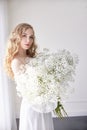 Curly blonde romantic look, beautiful eyes. White wildflowers in hands. Girl white light dress and curly hair, portrait of woman Royalty Free Stock Photo