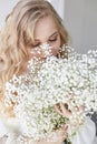 Curly blonde romantic look, beautiful eyes. White wildflowers in hands. Girl white light dress and curly hair, portrait of woman Royalty Free Stock Photo