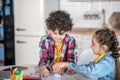 Curly boy and dark-haired girl sitting at round table, playing with alphabet letters, having fun Royalty Free Stock Photo