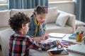 Curly boy and dark-haired girl sitting at round table, playing with alphabet letters, making words Royalty Free Stock Photo