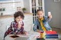 Curly boy and dark-haired girl sitting at round table, playing with alphabet letters, showing letters into the camera Royalty Free Stock Photo