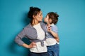 Curly brunette woman and her cute baby girl kissing while looking to each other on blue background Royalty Free Stock Photo