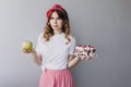 Curly caucasian girl thinking about her diet. Indoor shot of pensive wonderful lady holding green a