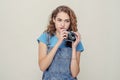 Curly cheerful brunette in denim overalls holds a film camera in her hands, having fun on the set