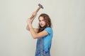 Curly cheerful brunette girl in denim overalls holds a hammer in her hand, lifts it over her head, swings