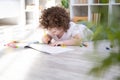 curly child girl drawing with colored markers lying on floor in living room at home