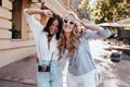 Curly debonair girl dancing with friend on the street. Outdoor photo of latin brunette woman having fun with sister..