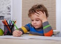 Curly European boy draws sitting at table