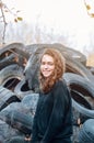 Curly girl with a beaming smile on the background of a pile of tires. Ecological problems