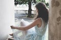 Curly girl in a light blue dress sitting in a pavilion in a garden. Side view