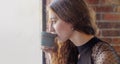 A curly girl with red hair poses in a cafe sipping from a cup of hot coffee look in profile.