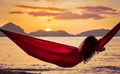 Curly young woman relaxing in a red hammock on a tropical island enjoying the sunset