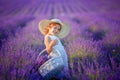 Curly girl standing on a lavender field in white dress and hat with cute face and nice hair with lavender bouquet and Royalty Free Stock Photo