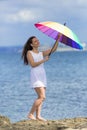 Curly girl in white sleeveless dress opens rainbow umbrella