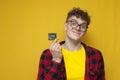 curly guy holds a condom on a yellow background and smiles, a student shows a contraceptive, the concept of safe sex