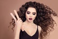 Curly hair. Beauty Close-up of brunette girl with blowing hairstyle holding straightening iron. Marsala eye shadow makeup.