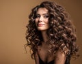 Curly Hair Model. Woman Wavy Long Hairstyle. Brunette Fashion Girl with Volume Hairdo and Natural Make up over Beige Background Royalty Free Stock Photo