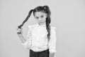 Curly hair ponytails for back to school. Adorable small girl twisting hair around her finger on yellow background. Cute