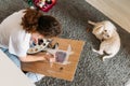 Curly hair smiling girl teenager in glasses in white t-shirt sitting on floor and painting on wooden desk with poodle dog at the Royalty Free Stock Photo