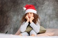 Curly haired beautiful uhappy tween girl in Santa hat and pajamas sitting on bed with pillow, christmas morning time