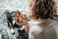 Curly cheerful woman with dog corgi sitting, relaxing and playing on floor at home. Weekend leisure activities