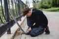 A curly-haired European teen in a black hoodie with skate sitting on the embankment and tying his shoelaces on sneakers Royalty Free Stock Photo