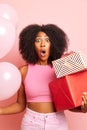 Curly haired funny woman with presents in a huge surprise next to pink wall