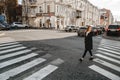 Curly-haired girl in a black coat crosses the street on the footpath