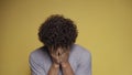 Curly-haired guy sobs with his hands covering his face. Man cries in the studio against an isolated background