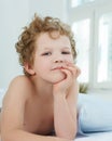 Curly-haired Caucasian little boy lying in bed propped up hands a head.