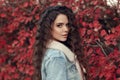 Curly haired Woman autumn outdoor portrait. Young beautiful brunette in jeans jacket with fur collar posing in red leaves park. A Royalty Free Stock Photo