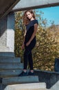 A curly-haired woman in black jeans stands on the stairs. Abandoned building