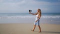 Female travel influencer records on pro camera with wireless lav mic on sandy beach. Curly-haired woman creates content