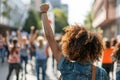 Curly-haired woman at protest, fist upraised, surrounded by other demonstrators in the city