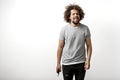 A curly-headed handsome man wearing a gray T-shirt is standing with a happy smile holding a phone in his hand over the Royalty Free Stock Photo