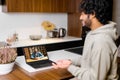 Side view at optimistic Indian man wearing hoodie sitting at desk and using laptop Royalty Free Stock Photo