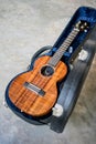 Curly koa ukulele gloss finished and hard case on concrete floor Royalty Free Stock Photo