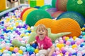 Curly little girl having fun in ball pit with colorful balls. Child playing on indoor playground. Kid jumping in ball Royalty Free Stock Photo