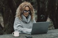 Curly long hair blonde adult woman use laptop computer outdoors sitting in the woods - concept of modern free female