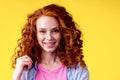 Curly redhaired ginger woman with snow white smile brackets on teeth touching a new hairstyle in studio yellow