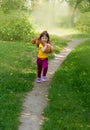 Curly smiling girl in a yellow T-shirt holds a large brown teddy bear on her neck and runs along the path Royalty Free Stock Photo