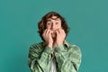 Curly teenager biting his nails in fear on color background