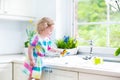 Curly toddler girl in colorful dress washing dishes